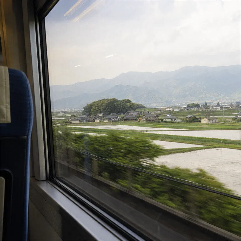 列車の車窓から見える田園と遠くの家並みの写真